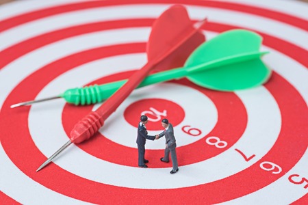 businessman make agreement on red and green darts on center of dartboard