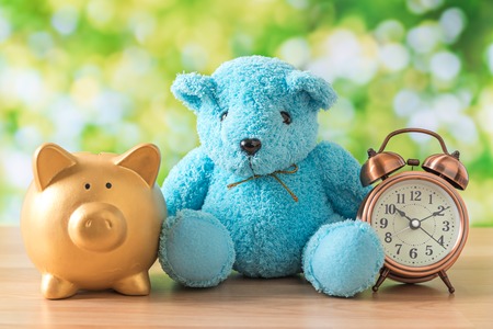blue bear doll sitting on wooden table with gold piggy bank and green natural bokeh backgroundの写真素材