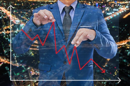 business man try to bring graph up when it falling down and night modern city building background , business conceptの写真素材