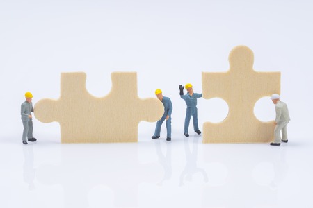 miniature people worker tring to connect jigsaw puzzle piecesの写真素材