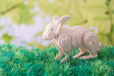 wooden rabbit on artificial green field and green leaves backgroundの写真素材