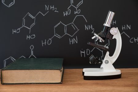 microscope and book on wooden table with science formula on black backgroundの写真素材