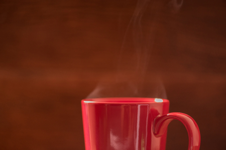 red coffee cup with smoke stream on wooden table under moring sunlight.の写真素材