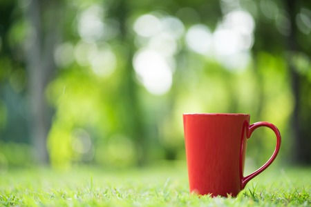 red coffee cup on green grass field in  morning timeの写真素材