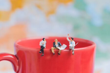 group of business miniature man sitting on red coffee cup edge with world map background.の写真素材