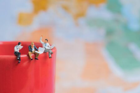 group of business miniature man sitting on red coffee cup edge with world map background.
