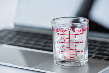 white pills in measuring cup on laptop computer background.の写真素材