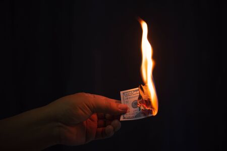 man hand holding burning dollar banknotes with fire on black backgroundの写真素材