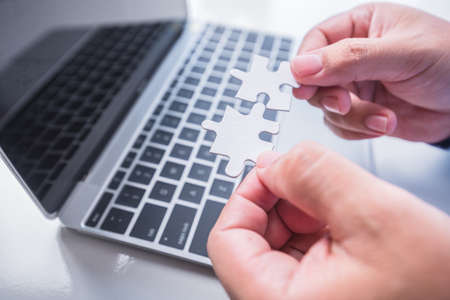 man hand connecting jigsaw puzzle pieces on laptop background