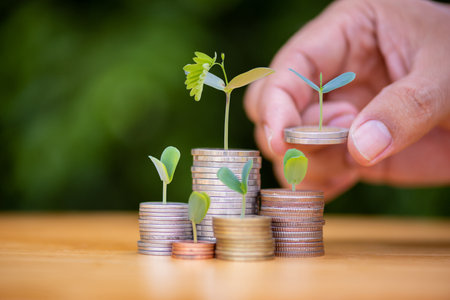 man hand putting coins on growing stack with plant growing on money . finance and accounting conceptの写真素材