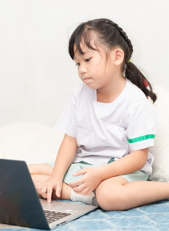 education, school, technology and internet concept - Cute girl with laptop pc at homeの写真素材