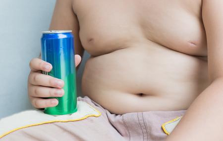 Diet. Obese fat boy holding soft drink can on gray backgroundの写真素材