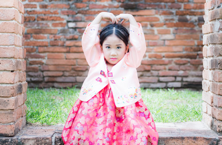 cute girl wearing Korea costumes show love symbol hand in park.の写真素材