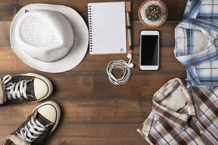 Travel preparations on wooden table, hat wallet, mobile-phone, notebook and shirt.の写真素材