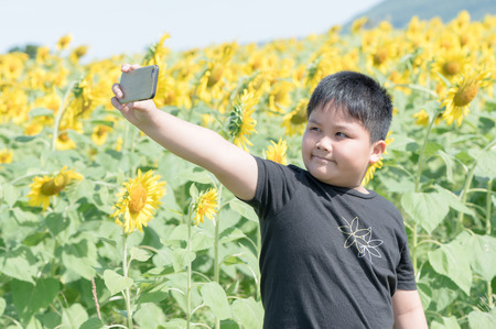Cute fat boy taking a selfie with smart phone on sunflowers background.の写真素材