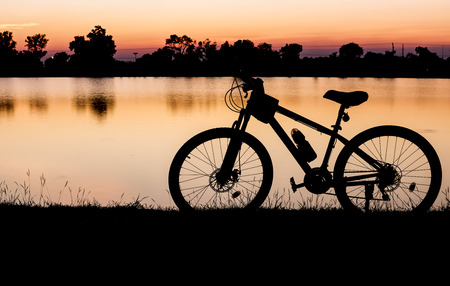 Silhouette bicycle on sunset and lake backgroundの写真素材