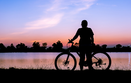 silhouette woman and  bicycle with lake on sunset background, relax and recreation concept..の写真素材