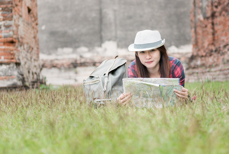 Beautiful woman traveler holding location map in hands and lying on the grass on archaeological  background, concept travel and leisure..の写真素材