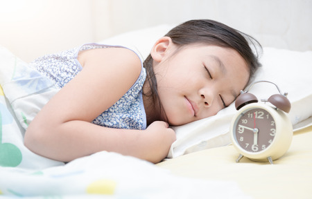 cute girl sleep on bed with alarm clock in morningの写真素材