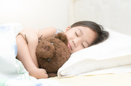 cute little asian girl sleep and hug teddy bear on bed in the bedroomの写真素材