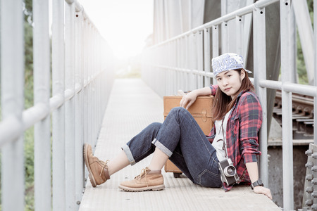 Hipster young girl sit on bridge railway with vintage luggage, concept travel and recreation.の写真素材