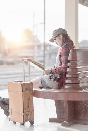 Hipster young girl holding map in hand and brown leather travel bag on railway station background, concept travel and leisure and vintage tone.の写真素材