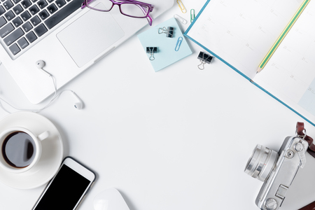 Modern white office desk table with laptop, mouse and other supplies with cup of coffee. Blank calendar notebook page. Top view, flat lay.の写真素材