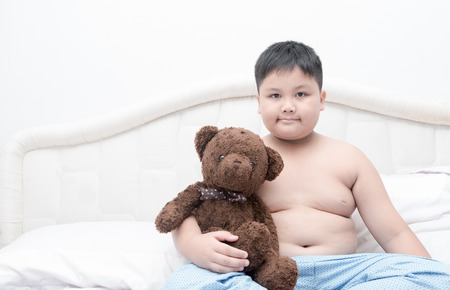 Obese fat boy hug teddy bear on bed, healthy care concept.の写真素材