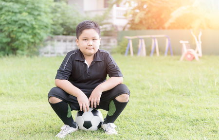 obese fat boy soccer player sit on football and green grass background, exercise concept.の写真素材