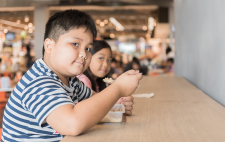 Obese brother and sister eating box lunch in food court, fastfood concept.の写真素材