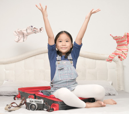 Happy cute girl throwing clothes and sit on suitcase, prepare travel conceptの写真素材