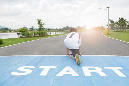 back side of fit and confident fat boy in starting position ready for running. kid athlete about to...
