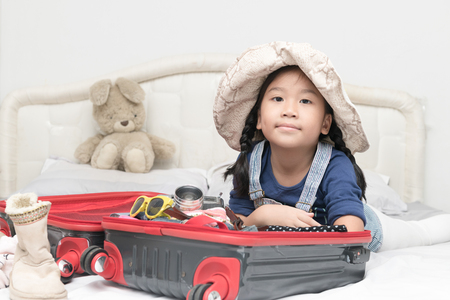 portrait of cute girl with travel accessories costumes. luggage, camera, sunglasses, clothes in suitcase on bed, prepared for the trip and travel concept.の写真素材