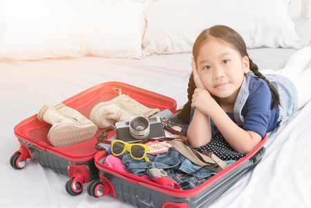 portrait of cute girl with travel accessories costumes. Passport, luggage, camera, sunglasses, clothes in suitcase on bed, prepared for the trip and travel concept.の写真素材