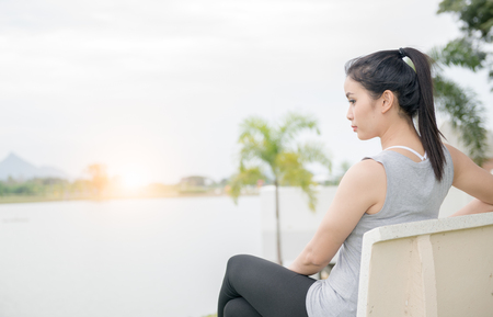 cute woman sit on chair near lake with sunrise, lonely concept.の写真素材