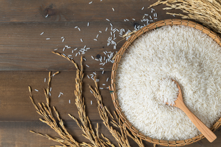 Thai jasmine rice on wood spoon in bamboo basket and on wood background top view and copy space, organic rice and healthy food.の写真素材