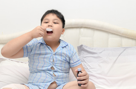 obese fat boy take syrup on bed because of the flu and cough, Health care concept..の写真素材