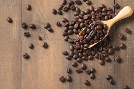 roasted coffee beans in wood scoop and on wood background, top view and copy space for text