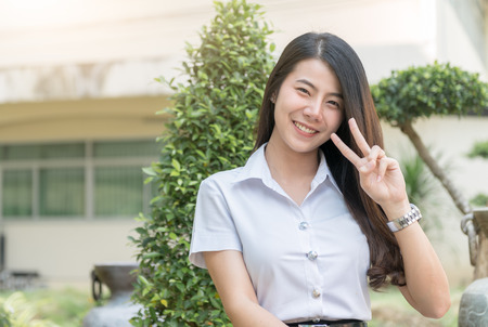 cute young asian woman in uniform student show v sign finber, smile and looking at camera, Happy and relax concept.の写真素材