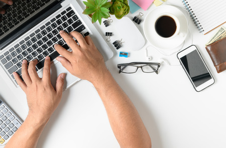 Business man typing laptop on modern white office desk table with smartphone and other supplies with cup of coffee on white background with Top view, flat lay.の写真素材