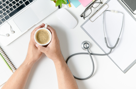 doctor hands with hot coffee working on table in the hospital. Medical concept..の写真素材