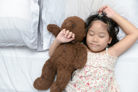 Cute little girl sleeps in the bed with a toy teddy bear, relaxation and rest conceptの写真素材