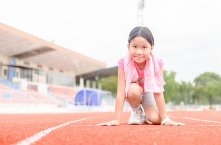 Cute girl in starting position ready for running. kid athlete about to start a sprint looking at camera with bright sunlight. diet and exercise concept.の写真素材