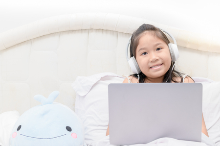 Cute girl play laptop and listening music from headphone, education concept.の写真素材