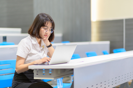 Asian student girl with glasses look at laptop while doing homework in classroom, education and technology internet concept.の写真素材