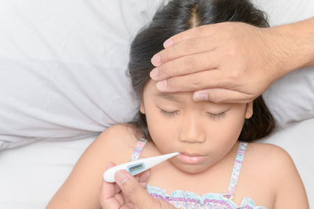 Father measuring temperature of ill kid. Sick child with high fever laying in bed and father holding...