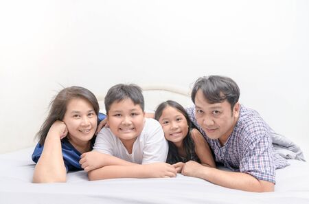 Asian Happy young family lying in bed together and looking at camera, warm and loving family concept.の写真素材