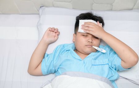 Sick boy with thermometer in mouth and compress on forehead.
