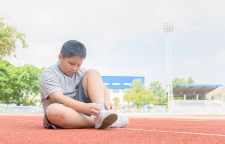Obese boy tying shoe laces prepare to run. Fat boy jogger getting ready for jogging on track. Exercise to lose weight.の写真素材