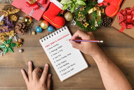Hand man writing New year resolution on note paper with decorations and gift boxes, New year and Merry christmas goal  conceptual.の写真素材